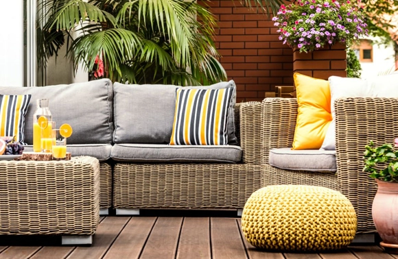 Un salon de jardin en rotin sur une terrasse en bois, avec des coussins. bleus et blancs.tapissier extérieur outdoor, rénovation meubles d'extérieur